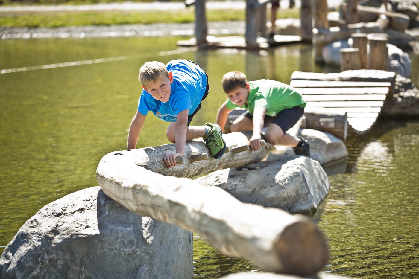Kinder balancieren über einen Holzsteg am Wasser – BIG Family Stubai